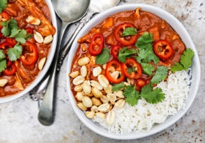 Sweet potato peanut stew served in a wide bowl over white rice, garnished with chopped cilantro and a lime wedge, warm overhead shot on a rustic wooden table
