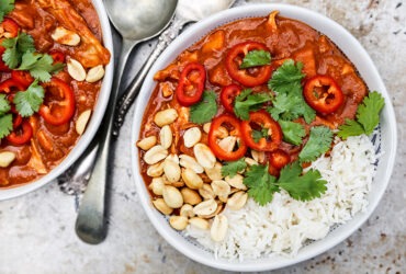 Sweet potato peanut stew served in a wide bowl over white rice, garnished with chopped cilantro and a lime wedge, warm overhead shot on a rustic wooden table