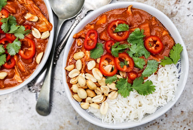 Sweet potato peanut stew served in a wide bowl over white rice, garnished with chopped cilantro and a lime wedge, warm overhead shot on a rustic wooden table