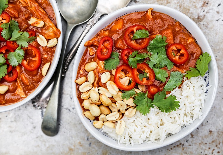 Sweet potato peanut stew served in a wide bowl over white rice, garnished with chopped cilantro and a lime wedge, warm overhead shot on a rustic wooden table