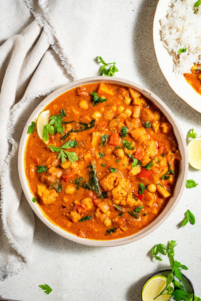 Flat lay of sweet potato peanut stew ingredients — sweet potatoes, chickpeas, peanut butter jar, crushed tomatoes, spices, onion, garlic, and ginger on a white surface