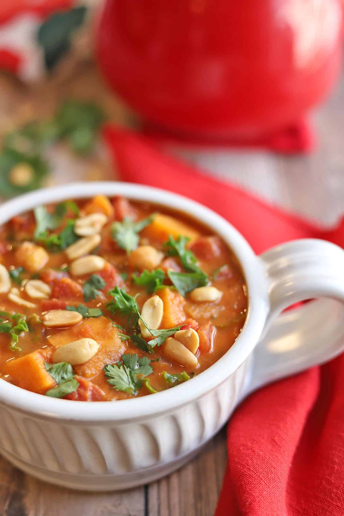 Close-up of a ladle lifting a scoop of sweet potato peanut stew from the pot, showing glossy peanut broth, chunks of sweet potato, and chickpeas with steam rising