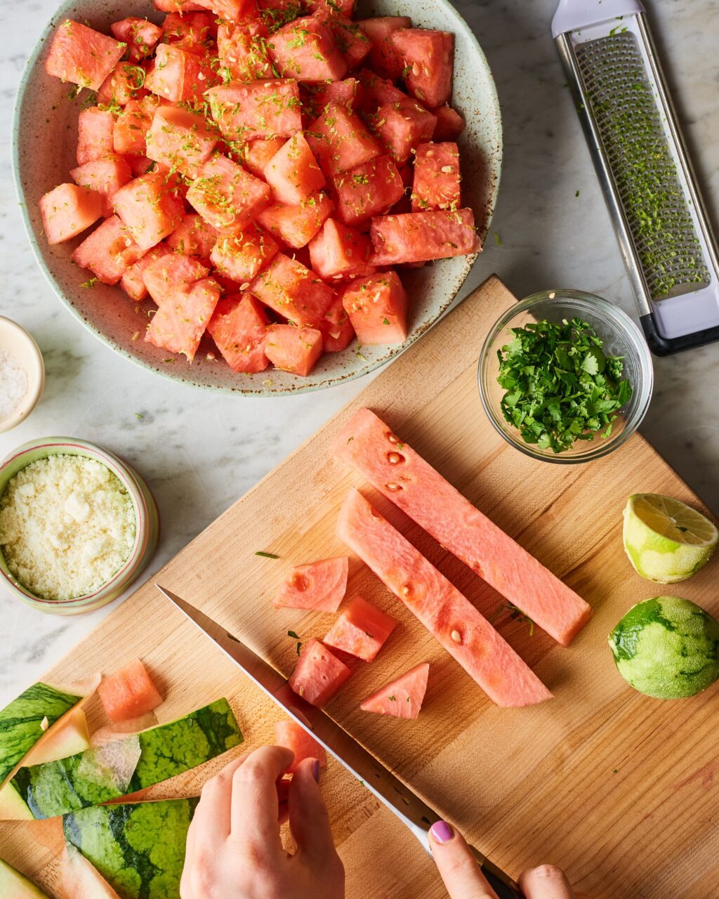 Cubed fresh watermelon pieces on a cutting board next to a blender, lime halves, and a small bowl of sugar — ingredients laid out for making watermelon sorbet