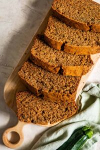 Sliced zucchini bread on a wooden cutting board with a golden-brown crust and moist crumb, warm cinnamon tones, overhead shot