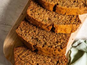 Sliced zucchini bread on a wooden cutting board with a golden-brown crust and moist crumb, warm cinnamon tones, overhead shot