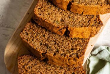 Sliced zucchini bread on a wooden cutting board with a golden-brown crust and moist crumb, warm cinnamon tones, overhead shot
