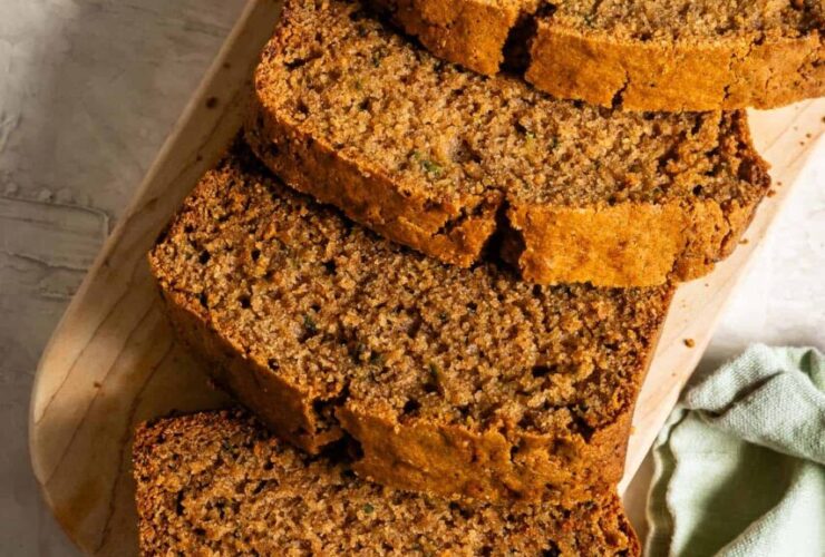 Sliced zucchini bread on a wooden cutting board with a golden-brown crust and moist crumb, warm cinnamon tones, overhead shot