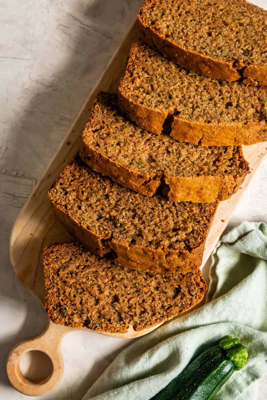 Sliced zucchini bread on a wooden cutting board with a golden-brown crust and moist crumb, warm cinnamon tones, overhead shot