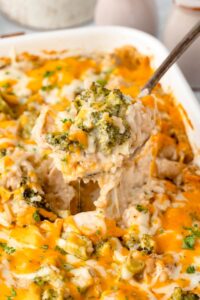 Chicken Broccoli Rice Casserole in a white baking dish with golden melted cheese on top, garnished with fresh parsley on a wooden dinner table