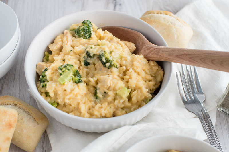 Overhead flat lay of chicken broccoli rice casserole ingredients including shredded rotisserie chicken, broccoli florets, shredded cheddar, cream of chicken soup, and uncooked rice on a white marble surface