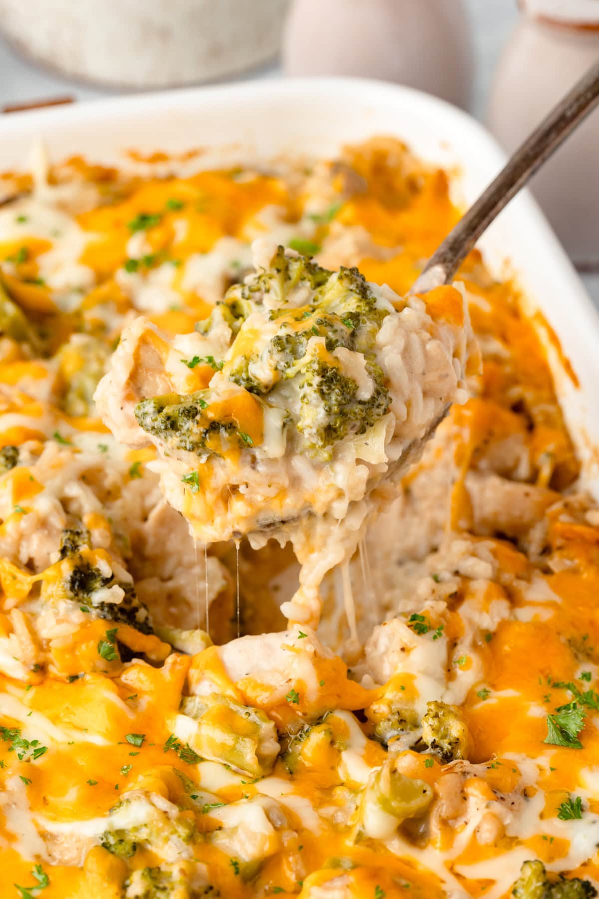 Close-up of a serving spoon lifting a cheesy portion of Chicken Broccoli Rice Casserole from the baking dish, showing the creamy interior with visible broccoli and shredded chicken