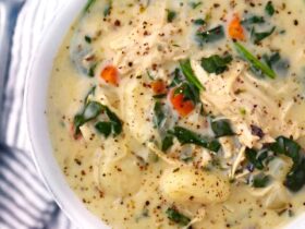 A bowl of creamy chicken gnocchi soup topped with fresh spinach and shredded carrots, served with crusty bread on a rustic wooden table