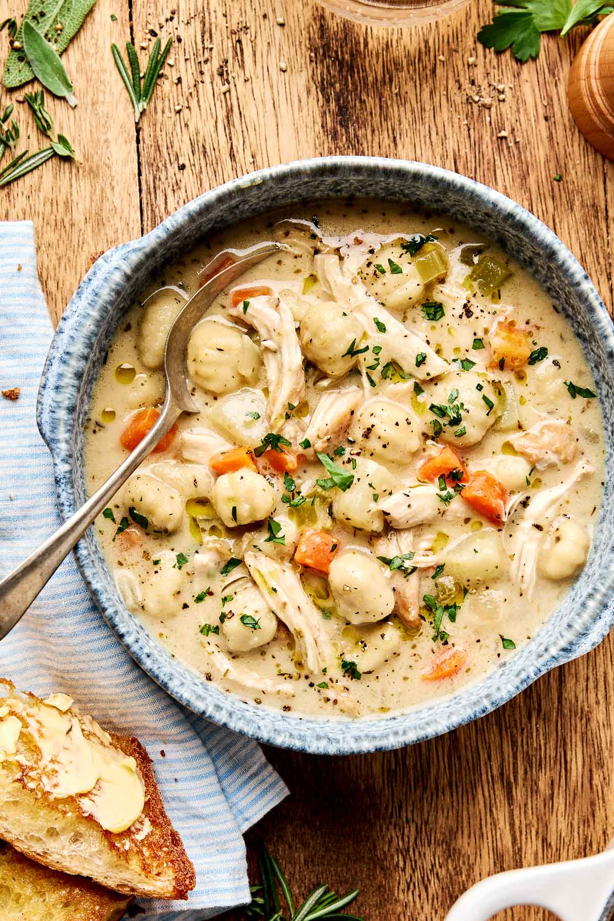 Overhead flat lay of chicken gnocchi soup ingredients including gnocchi, shredded carrots, spinach, rotisserie chicken, and cream on a marble surface