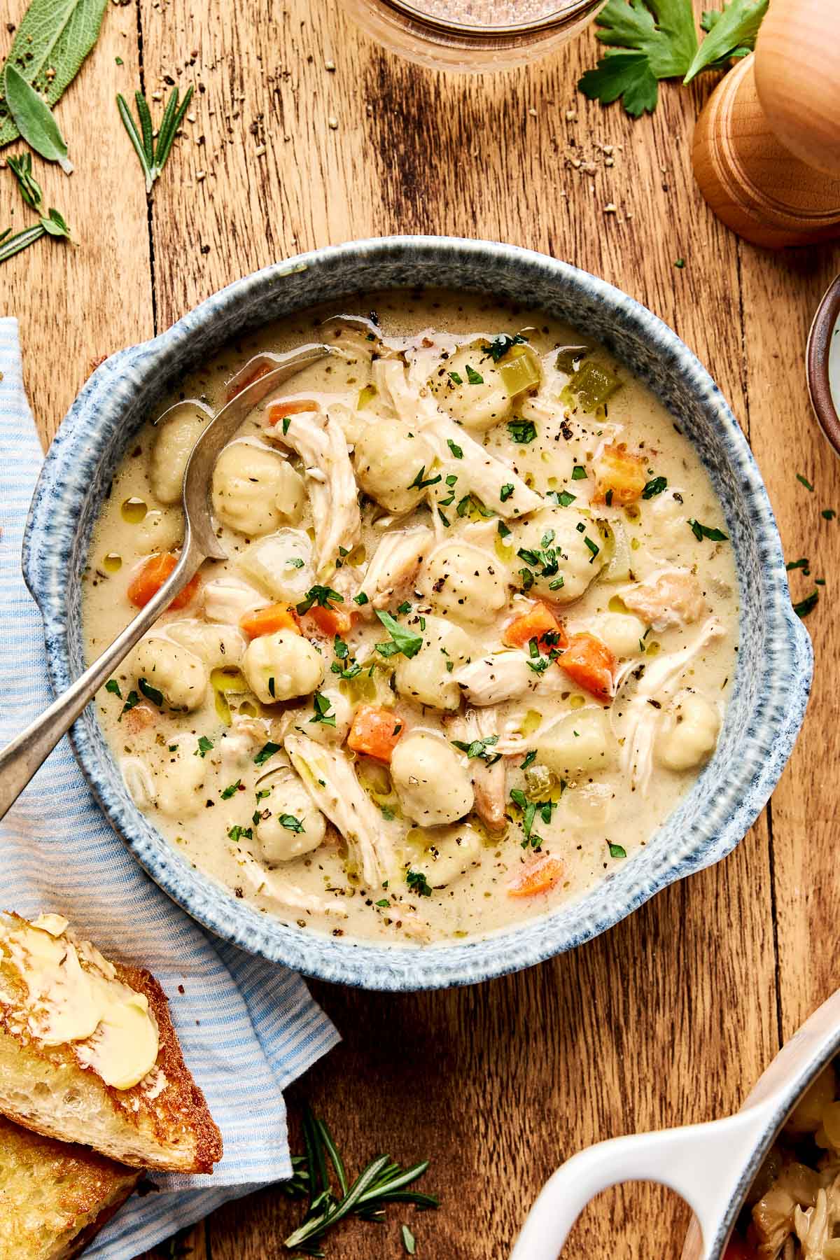 Close-up of a ladle lifting creamy chicken gnocchi soup from the pot, with visible pillowy gnocchi, shredded chicken, and wilted spinach