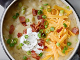 A rustic bowl of loaded baked potato soup topped with crispy bacon crumbles, shredded cheddar cheese, fresh chives, and a dollop of sour cream, styled on a wooden table with a linen napkin