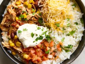 Slow Cooker Chicken Burrito Bowls served in a white bowl topped with sour cream, avocado slices, shredded cheese, and fresh cilantro