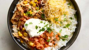 Slow Cooker Chicken Burrito Bowls served in a white bowl topped with sour cream, avocado slices, shredded cheese, and fresh cilantro