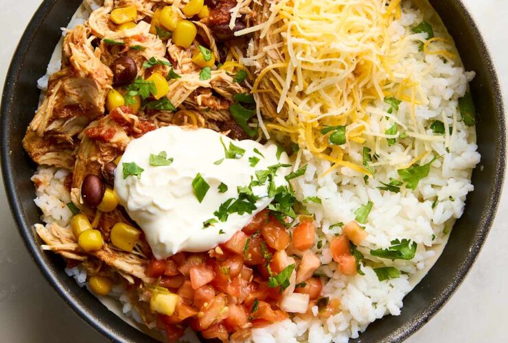Slow Cooker Chicken Burrito Bowls served in a white bowl topped with sour cream, avocado slices, shredded cheese, and fresh cilantro
