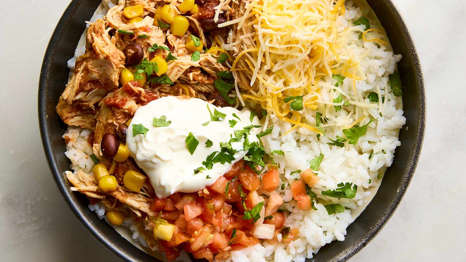 Slow Cooker Chicken Burrito Bowls served in a white bowl topped with sour cream, avocado slices, shredded cheese, and fresh cilantro