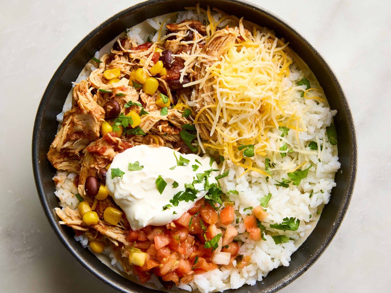 Overhead flat lay of slow cooker chicken burrito bowl ingredients including raw chicken thighs, canned black beans, frozen corn, enchilada sauce, rice, and spices arranged on a wooden surface