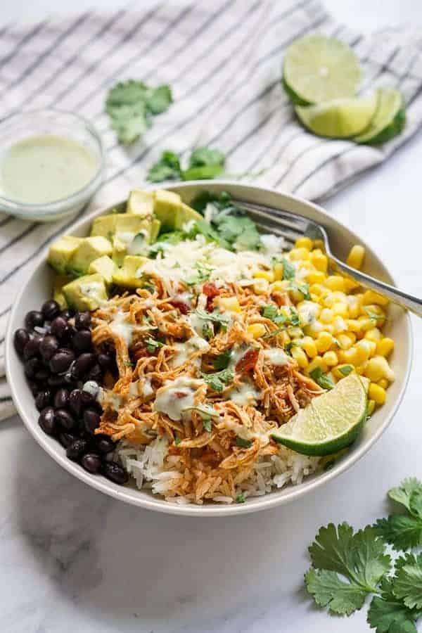 Close-up of a Slow Cooker Chicken Burrito Bowl with shredded chicken, rice, black beans, and corn topped with a dollop of sour cream, fresh lime wedge, and cilantro