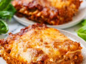 Slow cooker lasagna served on a white plate with a golden cheesy top, fresh basil garnish, and rich meat sauce visible in every layer