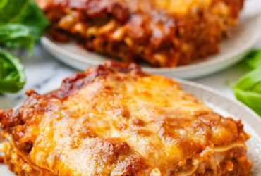 Slow cooker lasagna served on a white plate with a golden cheesy top, fresh basil garnish, and rich meat sauce visible in every layer