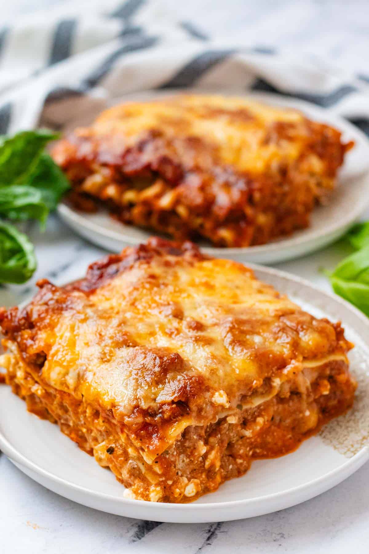Slow cooker lasagna served on a white plate with a golden cheesy top, fresh basil garnish, and rich meat sauce visible in every layer