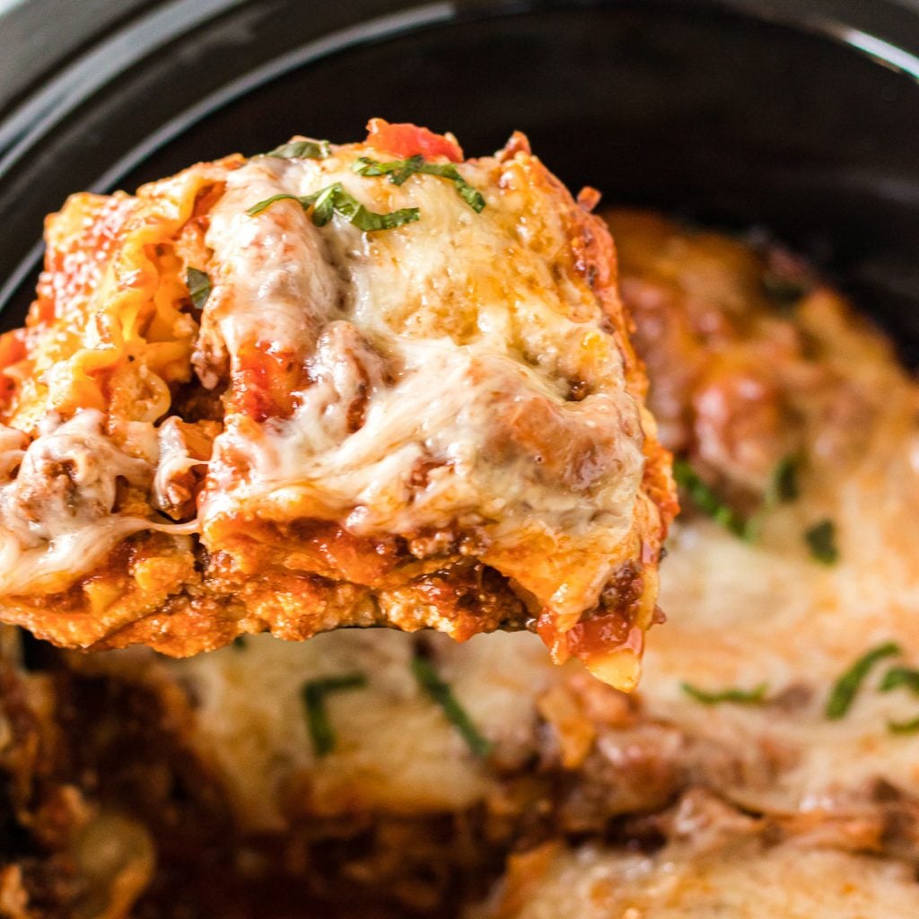 Close-up of a slice of slow cooker lasagna being lifted with a spatula, showing distinct layers of meat sauce, ricotta, and melted mozzarella cheese