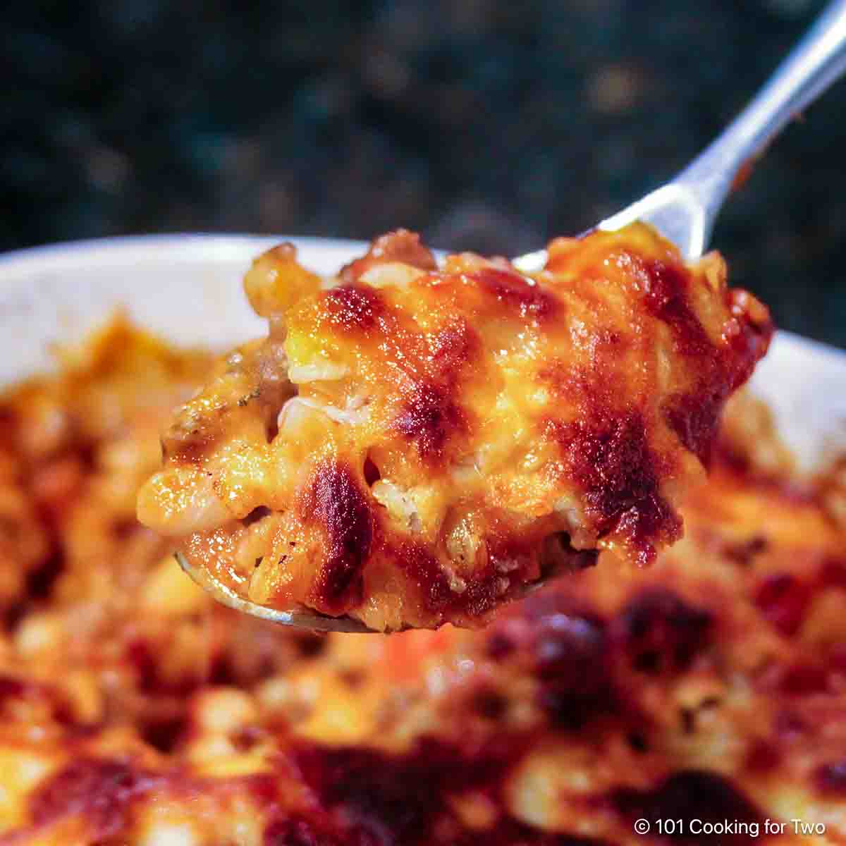 Close-up of a bowl of American goulash with tender elbow macaroni, ground beef, and tomato sauce, topped with shredded cheddar cheese