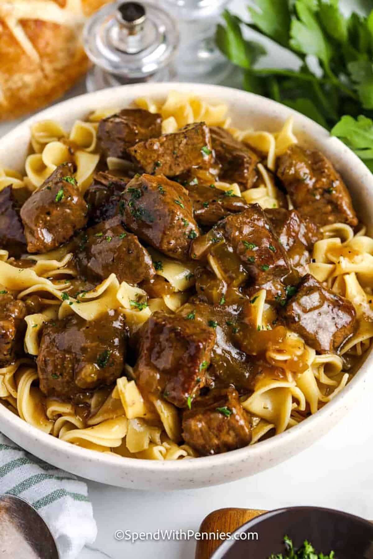 Close-up of a fork lifting shredded beef and wide egg noodles coated in glossy brown gravy from a rustic bowl