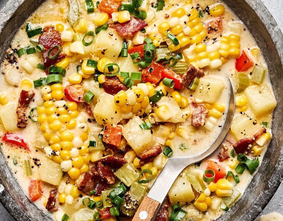 Side-by-side shot of raw corn chowder ingredients — diced potatoes, corn kernels, chopped bacon, onion, garlic, and cream — arranged on a cutting board next to a large pot