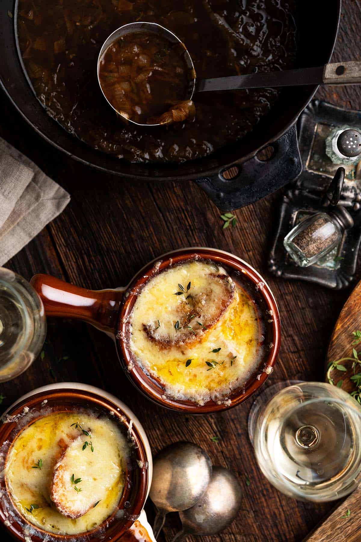 Classic French onion soup in a rustic ceramic crock with bubbling golden Gruyère and toasted baguette on top, served on a wooden table with a linen napkin