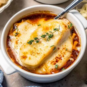 Close-up shot of a spoonful of French onion soup being lifted from a crock showing stringy melted Gruyère and dark caramelized onions in rich amber broth