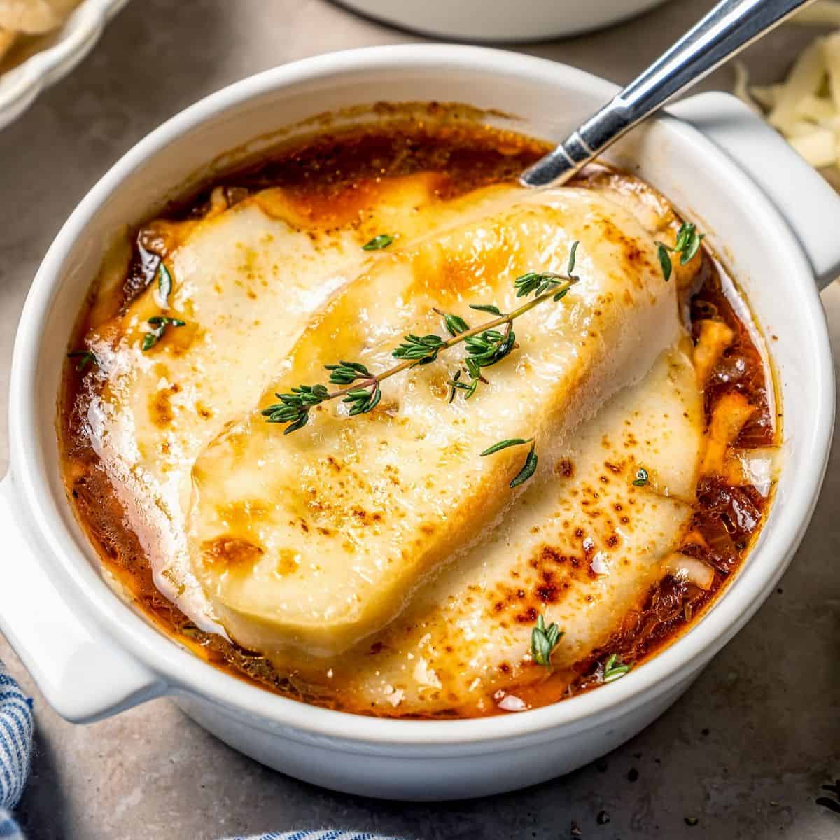 Close-up shot of a spoonful of French onion soup being lifted from a crock showing stringy melted Gruyère and dark caramelized onions in rich amber broth