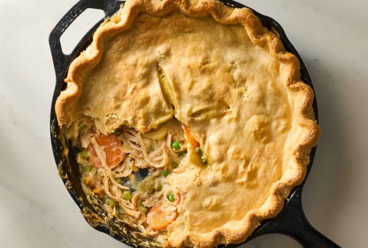 Golden flaky turkey pot pie in a cast iron skillet with a perfectly crimped crust and steam venting through slits, shot on a rustic wooden table with a serving spoon and golden-brown filling visible through a cut slice