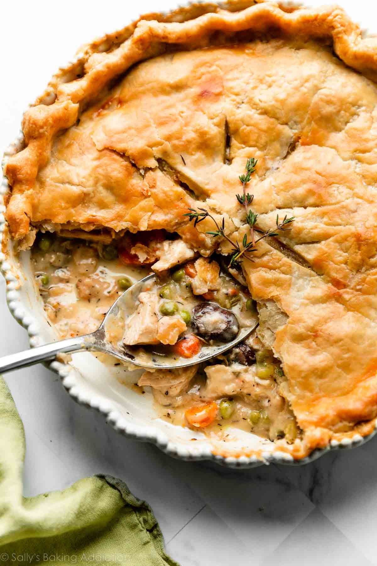 Overhead flat-lay of turkey pot pie ingredients: shredded turkey in a bowl, frozen mixed vegetables, a cup of leftover gravy, a tube of refrigerated pie crust, heavy cream, chicken broth, butter, flour, diced onion, and garlic on a white marble surface