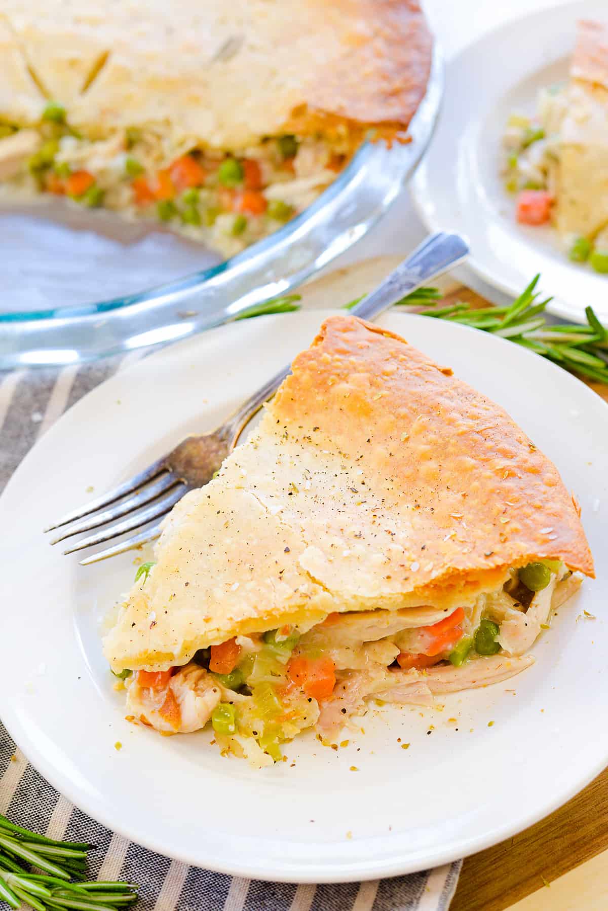 Close-up of a serving of turkey pot pie on a white plate showing the creamy golden filling with chunks of turkey, peas, carrots and corn spilling out from beneath the flaky, buttery top crust