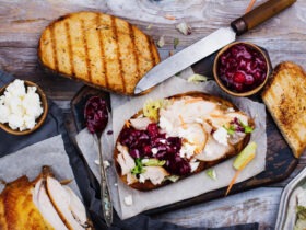 Leftover turkey sandwich with cranberry aioli on toasted sourdough, cut in half and stacked on a wooden cutting board with cranberry sauce on the side