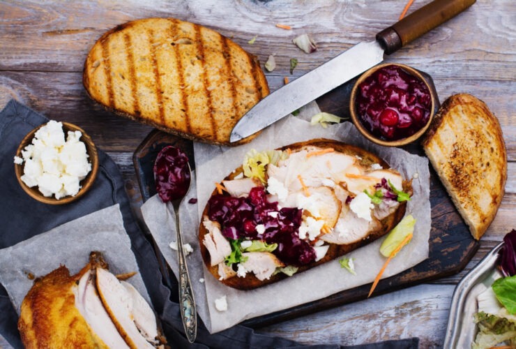 Leftover turkey sandwich with cranberry aioli on toasted sourdough, cut in half and stacked on a wooden cutting board with cranberry sauce on the side