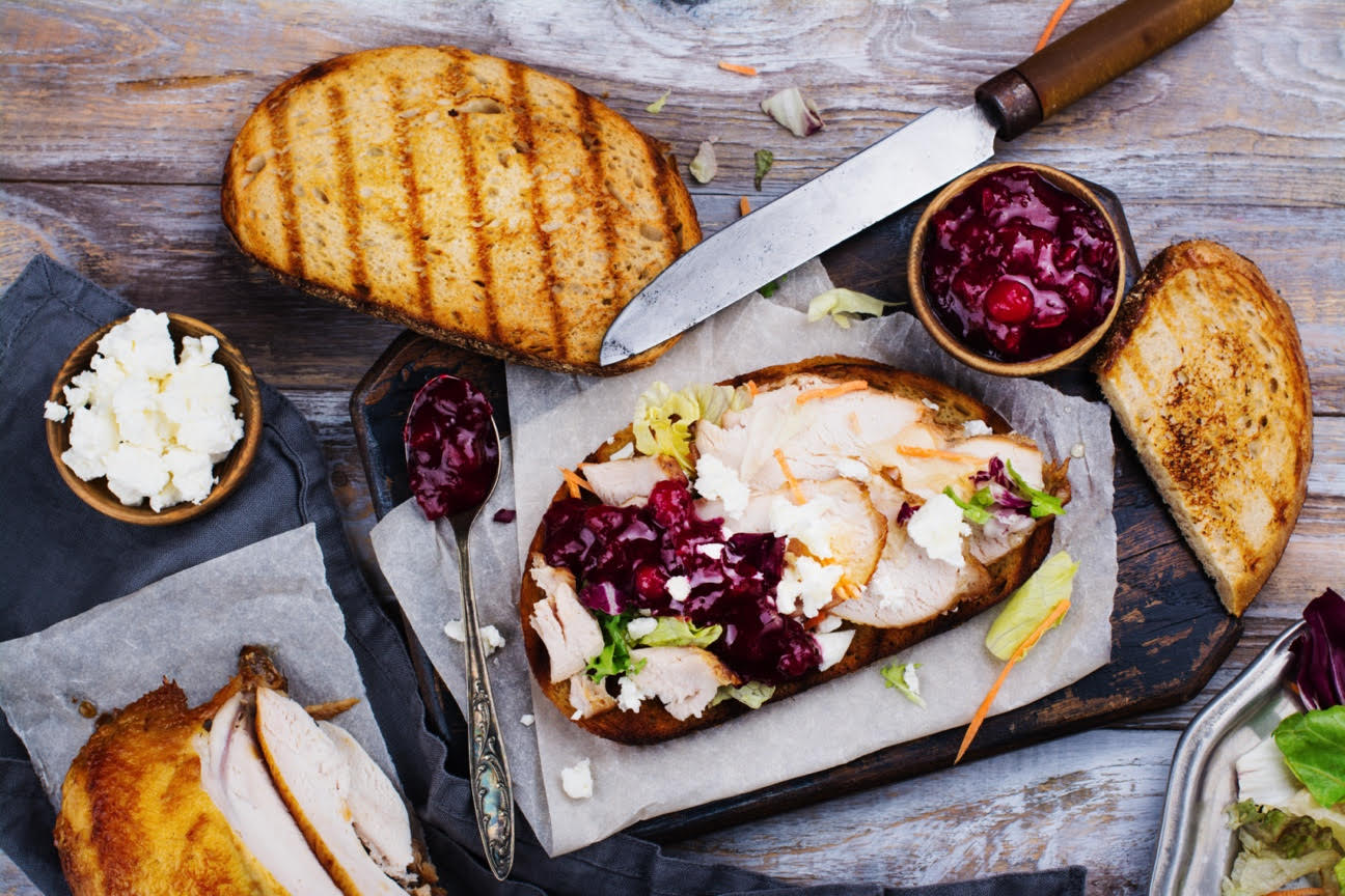 Leftover turkey sandwich with cranberry aioli on toasted sourdough, cut in half and stacked on a wooden cutting board with cranberry sauce on the side