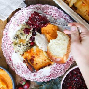 A flat-lay overhead shot showing prepped Thanksgiving ingredients organized on a kitchen counter: dried bread cubes, turkey stock in jars, cranberry sauce in a mason jar, pie crusts in pie dishes, fresh sage and thyme, and containers of prepped vegetables