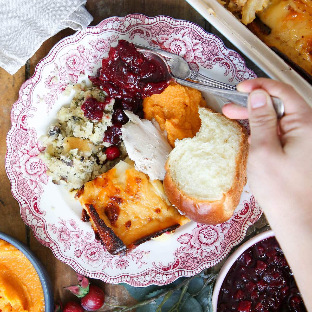 A flat-lay overhead shot showing prepped Thanksgiving ingredients organized on a kitchen counter: dried bread cubes, turkey stock in jars, cranberry sauce in a mason jar, pie crusts in pie dishes, fresh sage and thyme, and containers of prepped vegetables