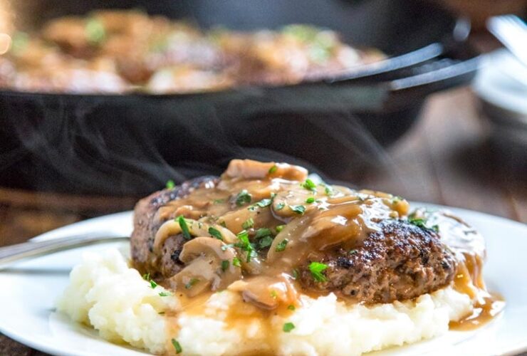 Salisbury steak beef patties smothered in rich onion mushroom gravy served over creamy mashed potatoes on a white dinner plate