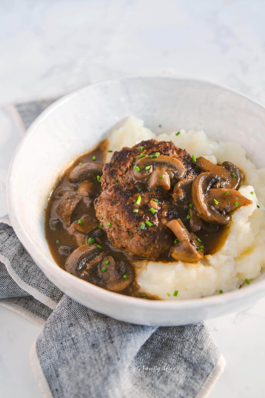 Close-up of Salisbury steak patty cut open over mashed potatoes showing juicy interior with mushroom onion gravy spooned over the top