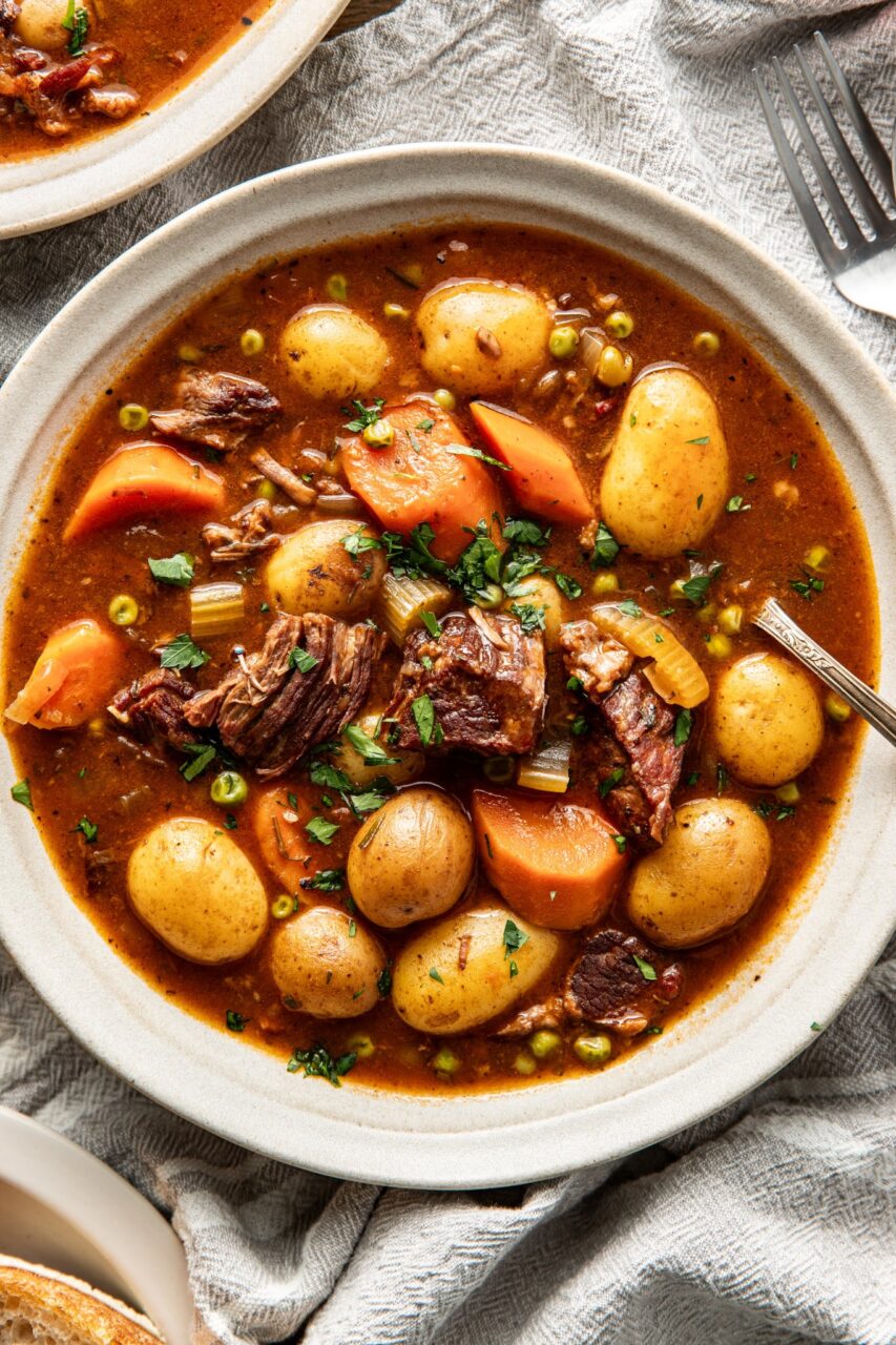 Slow cooker beef stew served in a white bowl with fork-tender chunks of beef, golden potatoes, and bright orange carrots in a rich dark herb gravy, garnished with fresh parsley