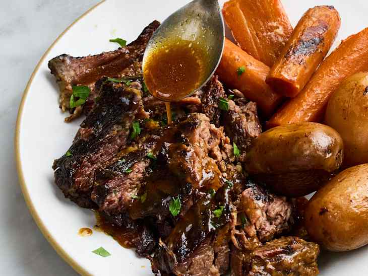 Slow cooker pot roast with tender chuck roast, carrots, potatoes, and onions on a white serving platter with rich brown gravy poured over top