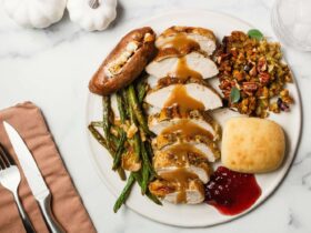 A beautifully plated Thanksgiving dinner for two with sliced herb-butter turkey breast, golden stuffing, mashed potatoes with a butter pool, green bean casserole, and cranberry sauce arranged on a rustic wooden table with candles