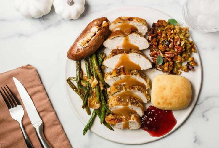 A beautifully plated Thanksgiving dinner for two with sliced herb-butter turkey breast, golden stuffing, mashed potatoes with a butter pool, green bean casserole, and cranberry sauce arranged on a rustic wooden table with candles