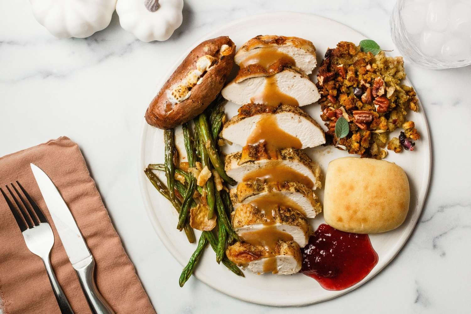 A beautifully plated Thanksgiving dinner for two with sliced herb-butter turkey breast, golden stuffing, mashed potatoes with a butter pool, green bean casserole, and cranberry sauce arranged on a rustic wooden table with candles